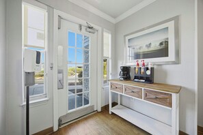 Una habitación con una puerta blanca, una ventana, una cafetera y un cuadro en la pared.