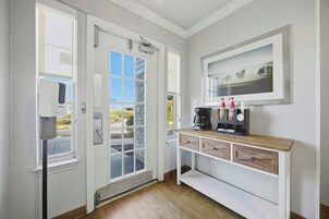 Una habitación con una puerta blanca, una ventana, una cafetera y un cuadro en la pared.