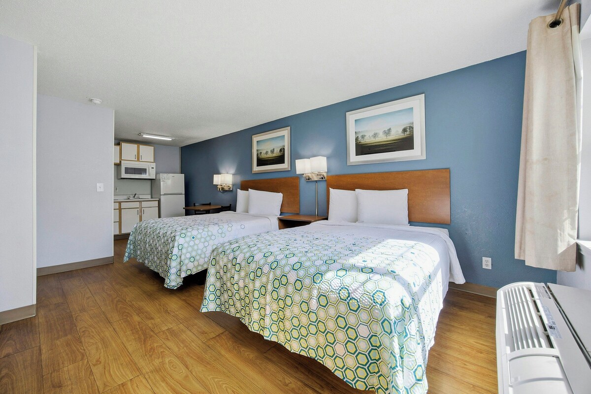 A hotel room with two beds, a kitchenette, and a view of the outdoors.