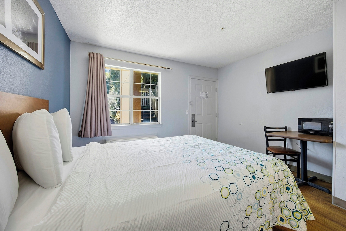 A hotel room with a bed, a desk, a chair, a TV, and a window with curtains.