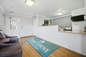 Un área de recepción con mostrador, televisor de pantalla plana, una puerta y zona de estar con sillones de cuero.