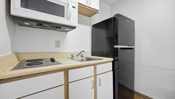 A kitchen with a microwave, stove, sink, and black refrigerator.