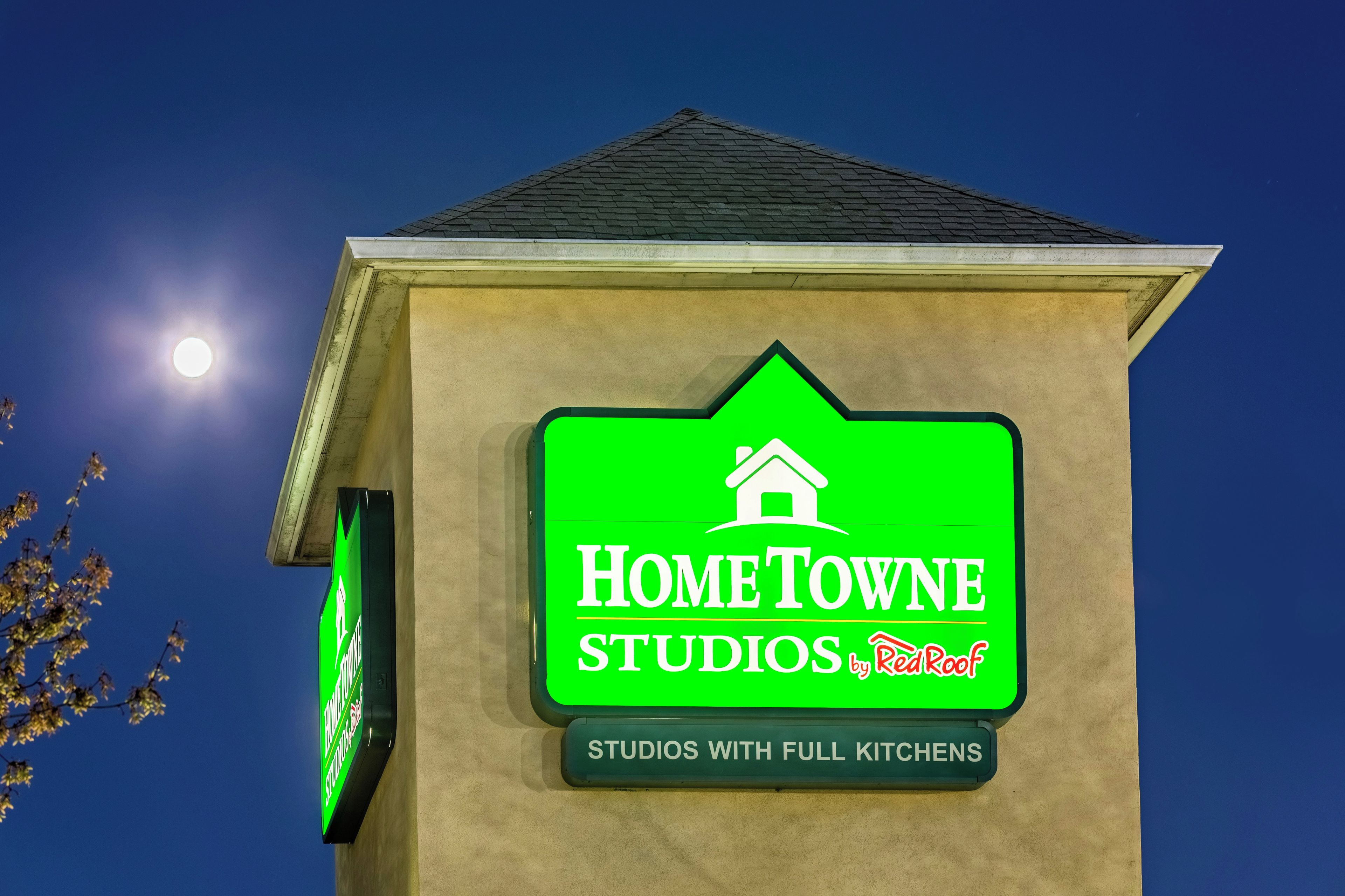 Un edificio con un letrero verde que dice 'HomeTowne Studios by RedRoof' e indica que cuenta con cocinas completas.