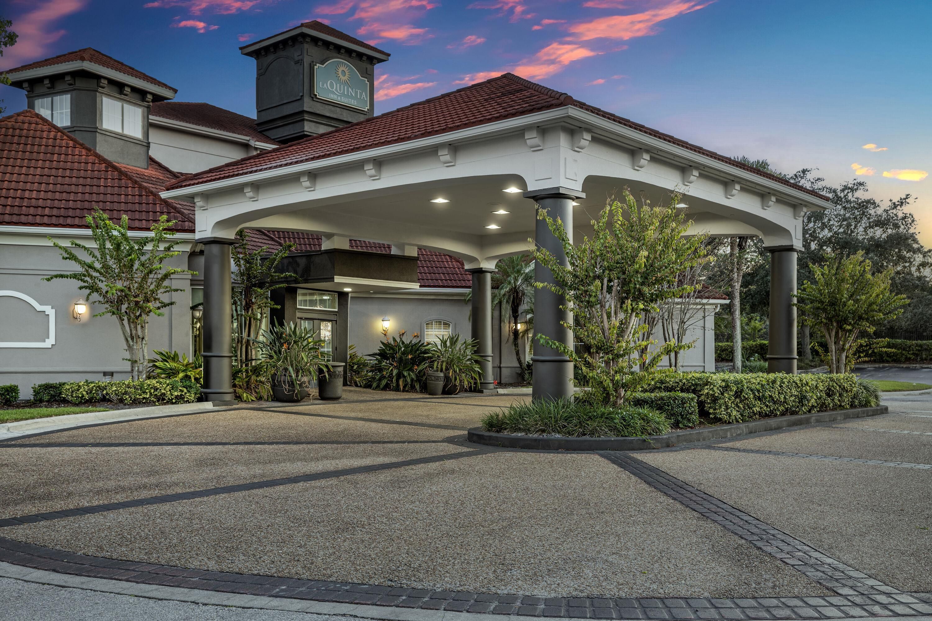A hotel entrance with a covered walkway, potted plants, and a clear sky.