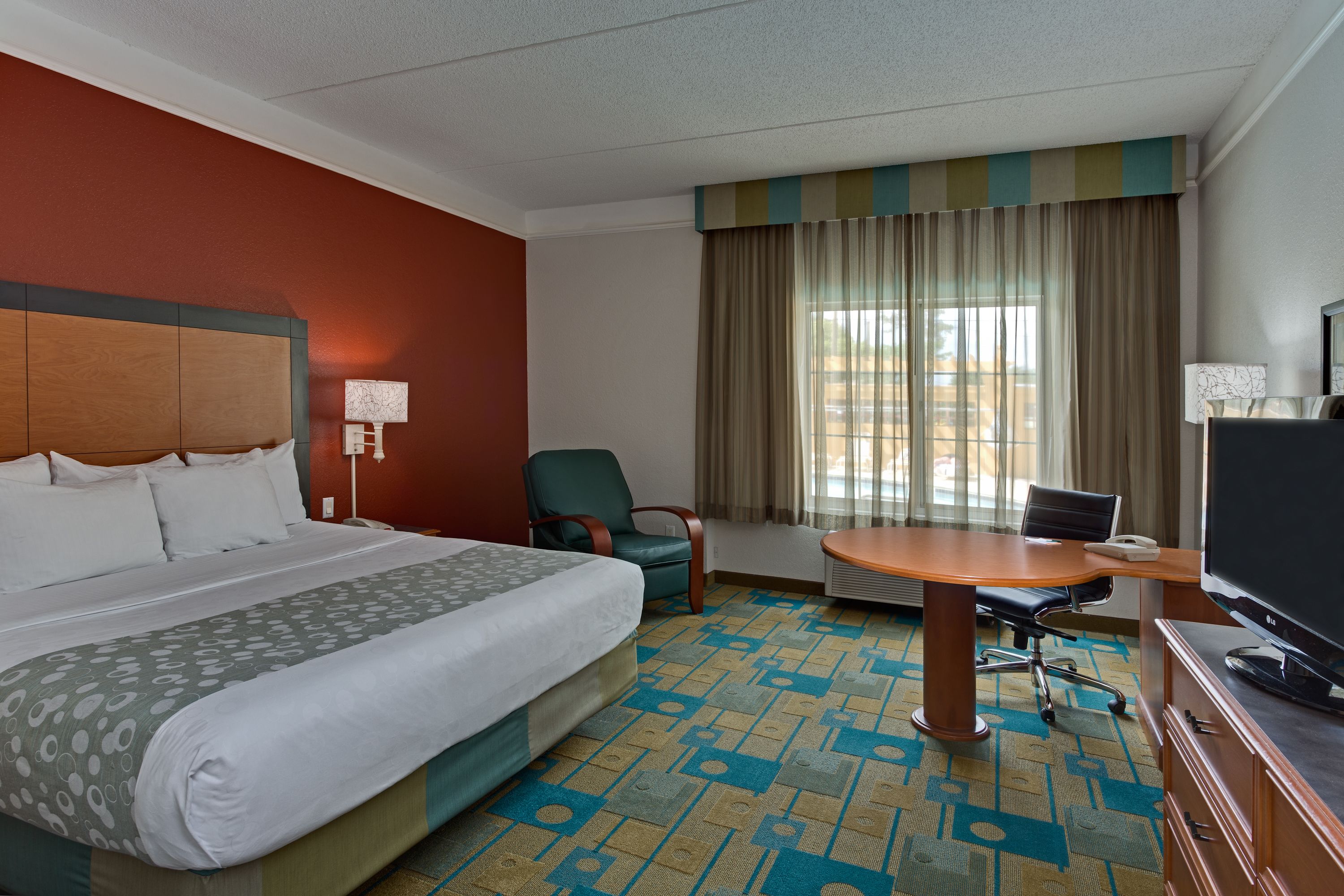 A hotel room with a large bed, a desk with a TV, a chair, and a window with curtains.