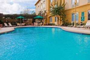 A swimming pool with lounge chairs and umbrellas, surrounded by a building with a yellow facade and multiple windows. - La Quinta Inn & Suites by Wyndham USF (Near Busch Gardens) (Tampa)
