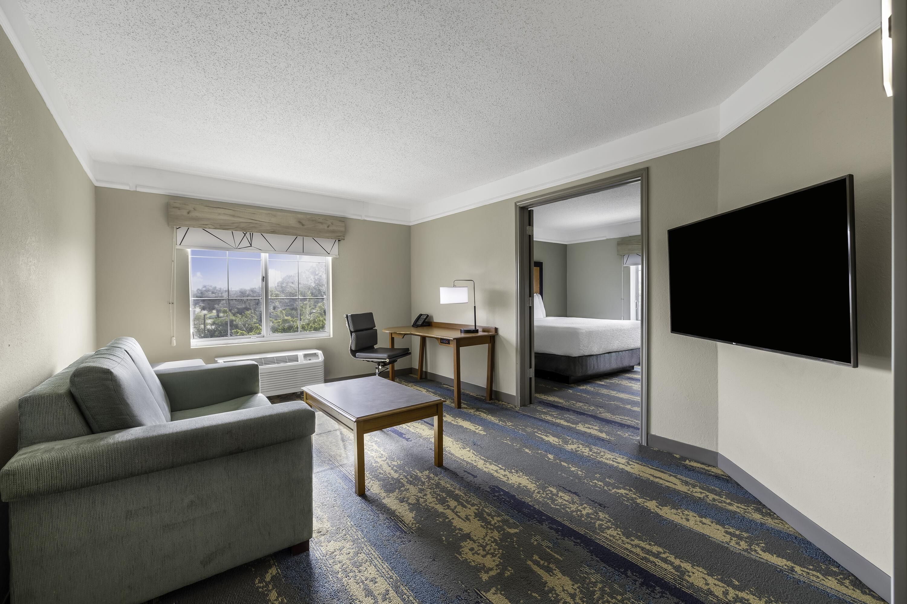 A hotel room with a sofa, a desk, a flat-screen TV, and a bed.