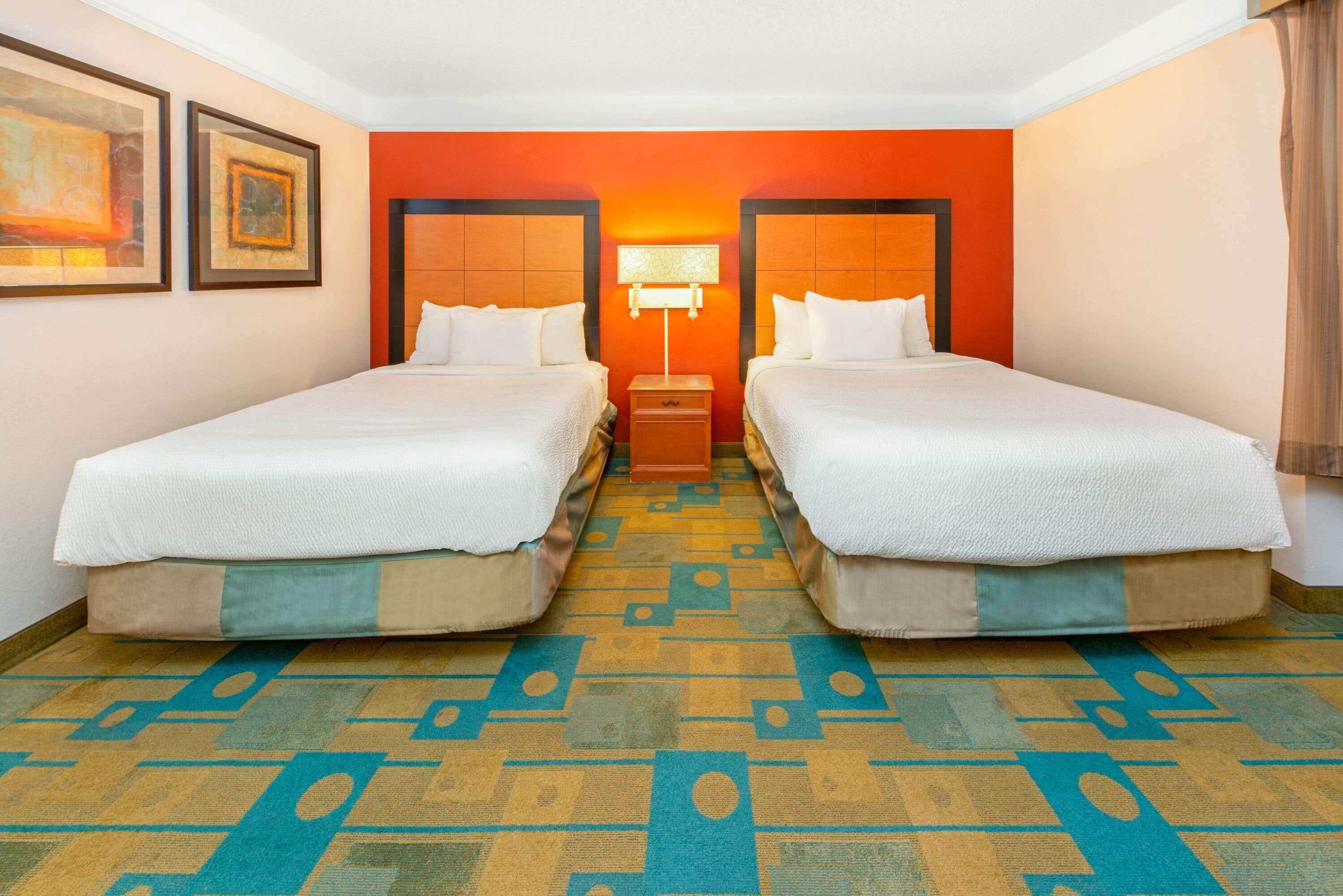 A hotel room with two beds, a patterned carpet, and a wall with framed artwork.