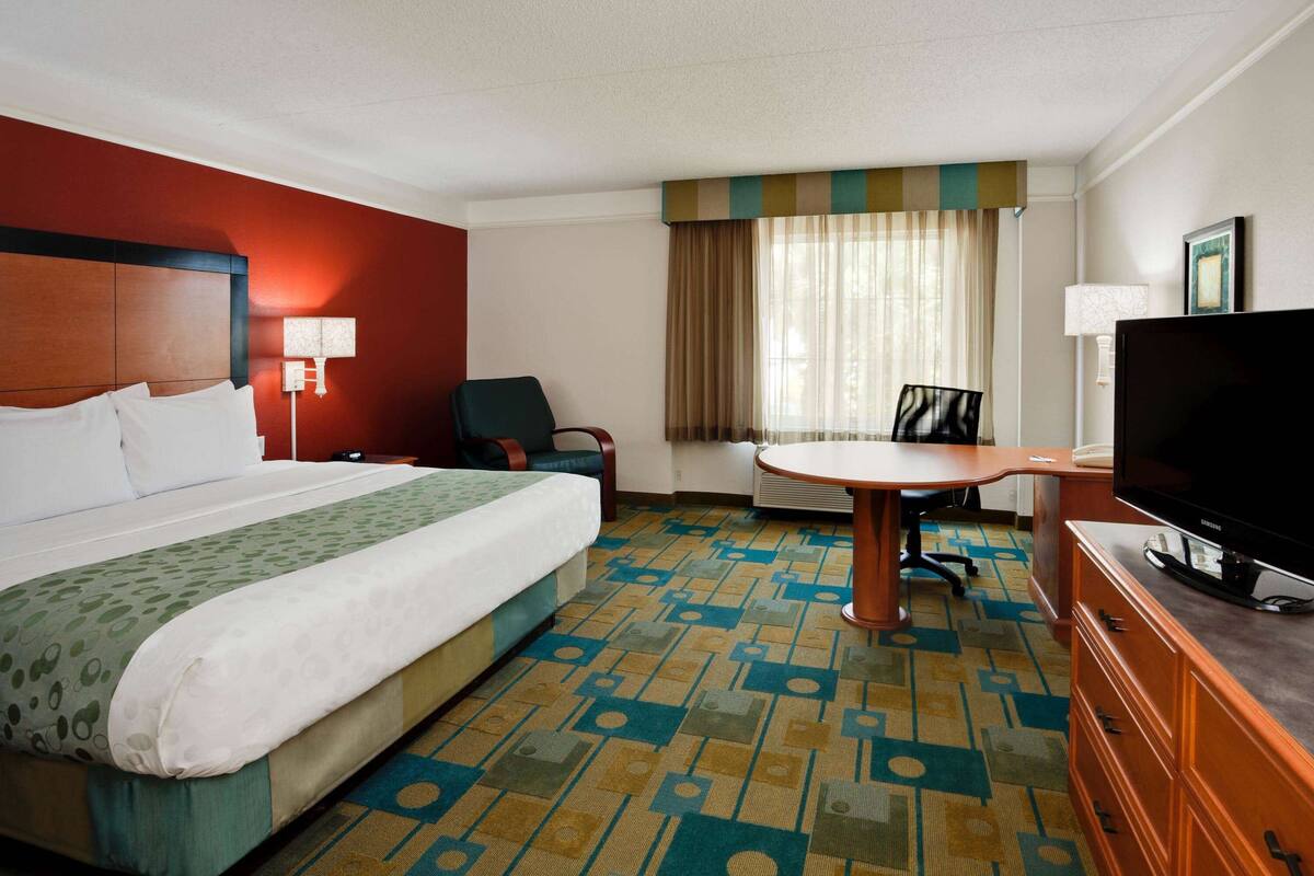 A hotel room with a large bed, a desk, a chair, a television, and a window with curtains.