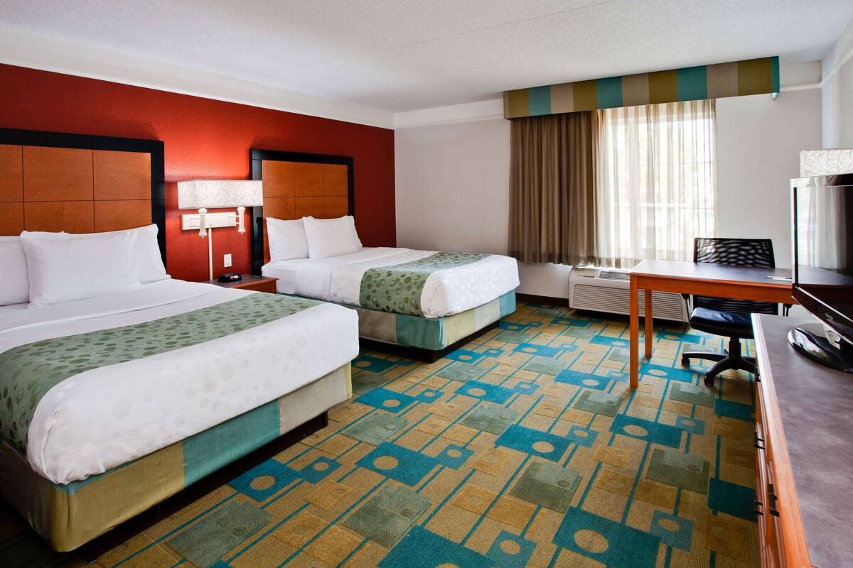 A hotel room with two beds, a desk, a television, and a window with curtains.