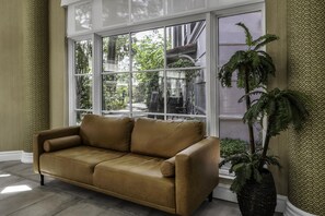 A room with a large window, a brown leather sofa, and a potted plant. - La Quinta Inn & Suites by Wyndham USF (Near Busch Gardens) (Tampa)