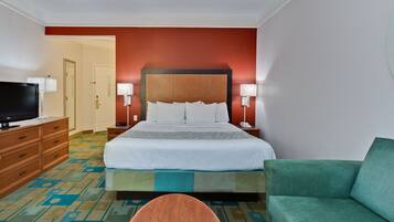 Habitación de hotel con una cama grande, un televisor sobre una cómoda de madera, un sofá verde y una alfombra estampada.
