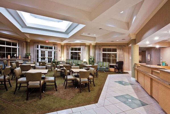A spacious hotel lobby with multiple seating areas, a reception desk, and a skylight ceiling. - La Quinta Inn & Suites by Wyndham USF (Near Busch Gardens) (Tampa)