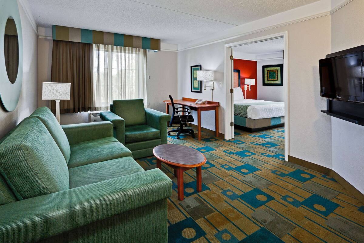 A hotel room with a green sofa, a small table, a desk, and a bed.