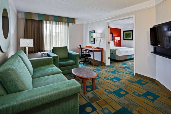 A hotel room with a green sofa, a small table, a desk, and a bed. - La Quinta Inn & Suites by Wyndham USF (Near Busch Gardens) (Tampa)