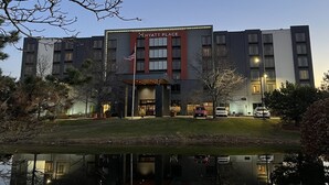 Un hotel Hyatt Place con una fachada moderna, una bandera estadounidense y un reflejo en el agua.