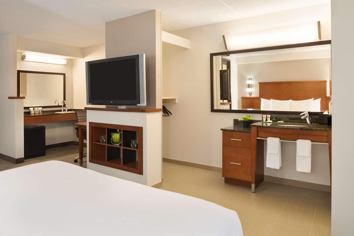 A hotel room with a bed, a TV, a bathroom with a mirror, and a sink.