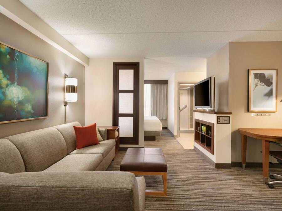 A hotel room with a sofa, a small table, a TV, a desk, and a cabinet with shelves.