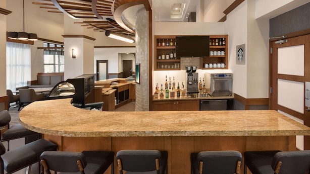 Zona de bar moderna con mostrador curvo de granito, taburetes y una variedad de botellas de licor.