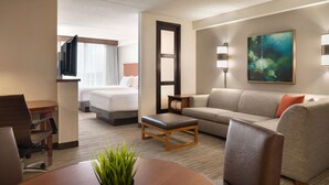 Habitación de hotel con cama, sofá, mesa de centro, televisión y un cuadro en la pared.