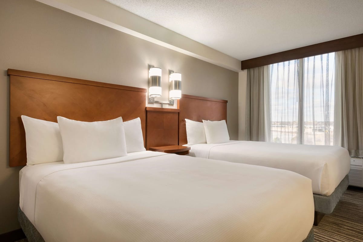 A hotel room with two beds, a wooden headboard, a nightstand, and a large window with curtains.