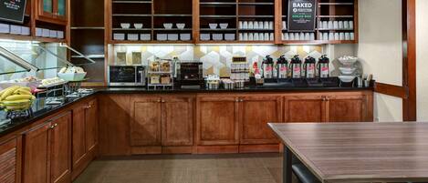 A kitchen with wooden cabinets, a counter with food items, and a coffee station.