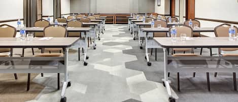A conference room with multiple tables and chairs, equipped with water bottles and glasses.
