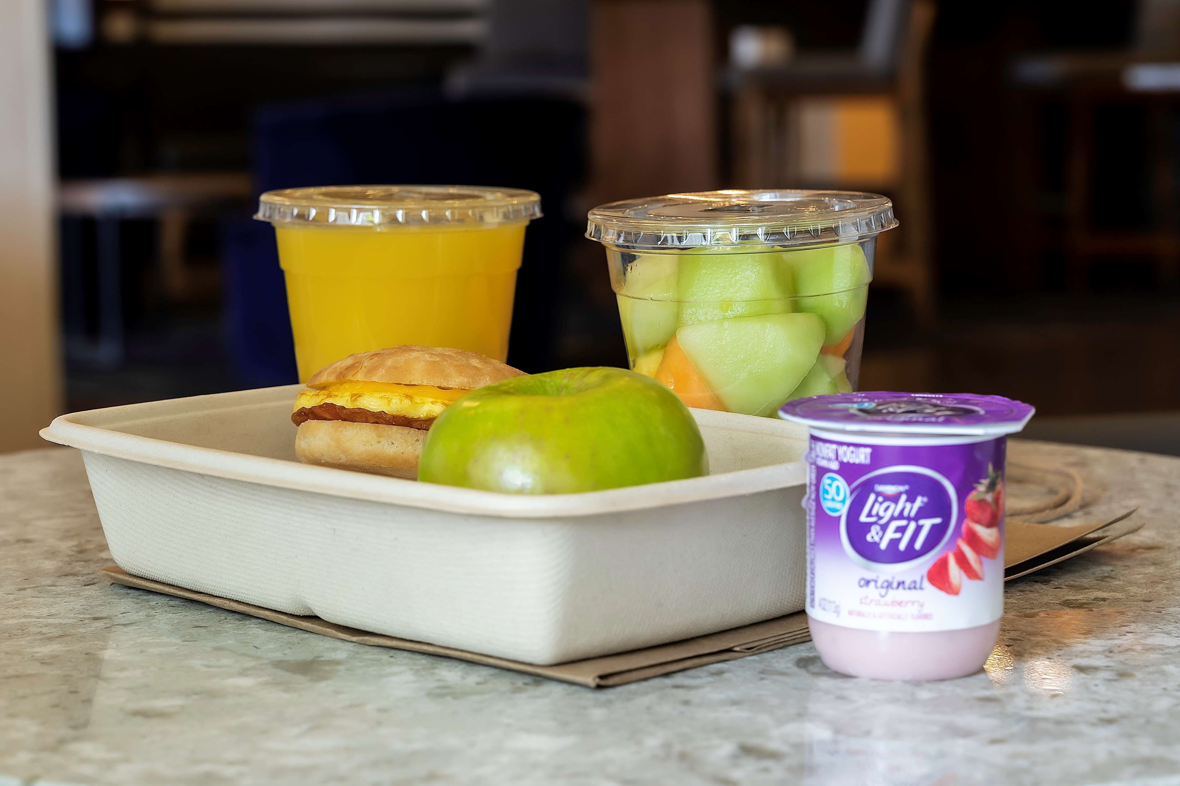 A meal tray with a croissant, apple, and a container of yogurt.
