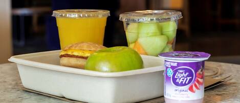 A meal tray with a croissant, apple, and a container of yogurt.