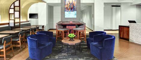 A modern lobby with a round table, blue armchairs, and a flat-screen TV mounted on the wall.
