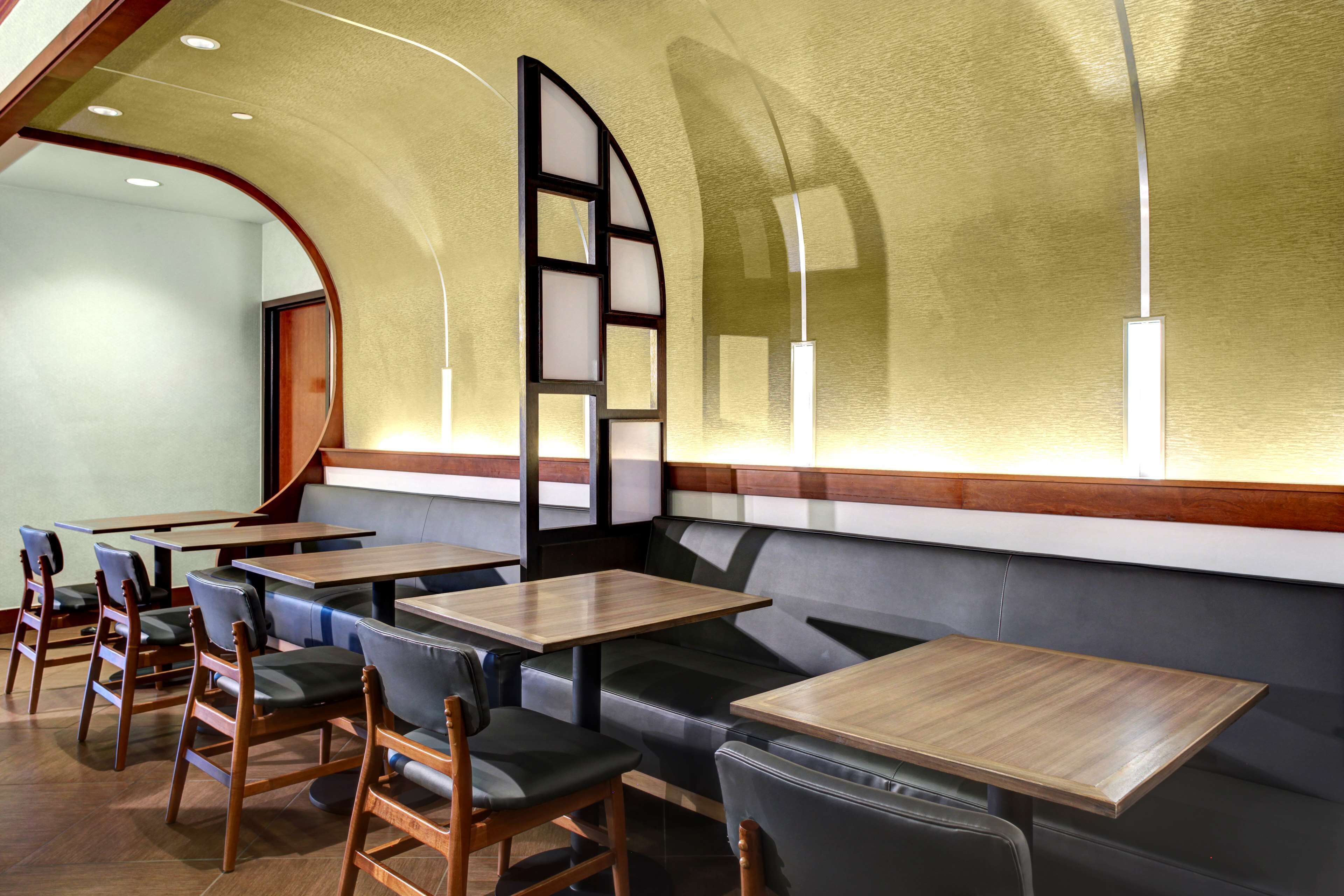 A restaurant interior with wooden tables and chairs, a curved wall, and a seating area with a cushioned bench.