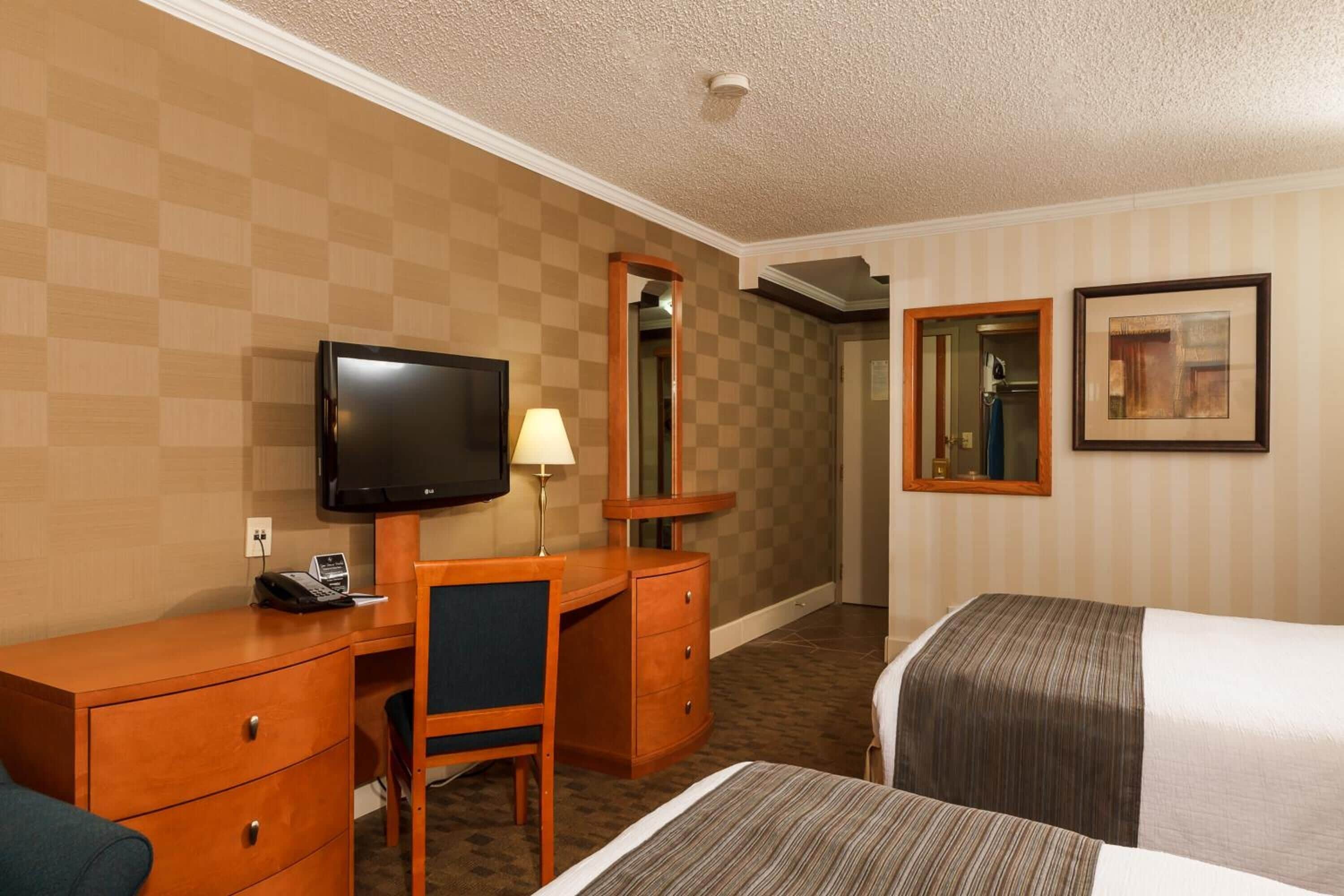 Ein Hotelzimmer mit Schreibtisch, Stuhl, Fernseher, zwei Betten, einem Spiegel und einem gerahmten Bild an der Wand.