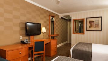 Ein Hotelzimmer mit Schreibtisch, Stuhl, Fernseher, zwei Betten, einem Spiegel und einem gerahmten Bild an der Wand.