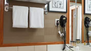A bathroom with a toilet, a sink with a mirror, a towel rack with towels, and a hairdryer on the wall.