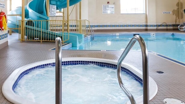 Una piscina interior con un jacuzzi, un tobogán de agua azul y una escalera que lleva a una plataforma superior.