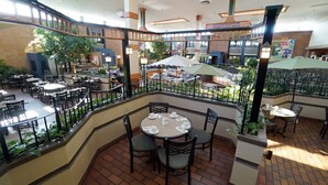 Un comedor amplio en el interior con varias mesas y sillas, rodeado por un balcón con barandillas y plantas en macetas.