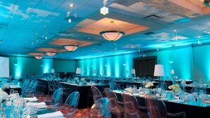 Un amplio salón de conferencias con filas de sillas transparentes, mesas dispuestas para comer y una iluminación azul ambiental.