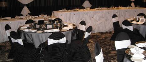 Uma sala de banquetes com mesas redondas preparadas para um evento formal, cada uma com louça e copos.