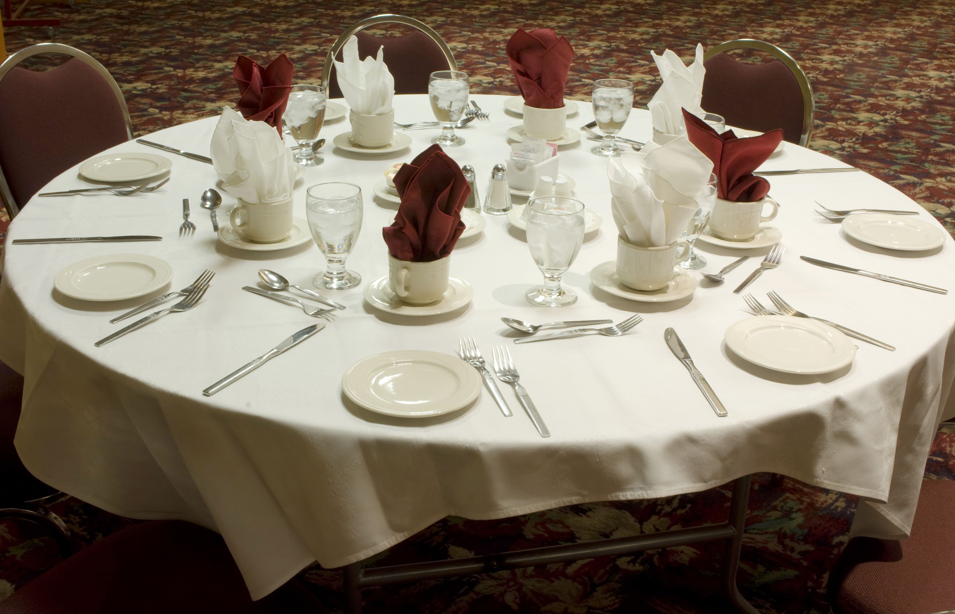 A round dining table set with white tablecloth, plates, cutlery, and napkins.
