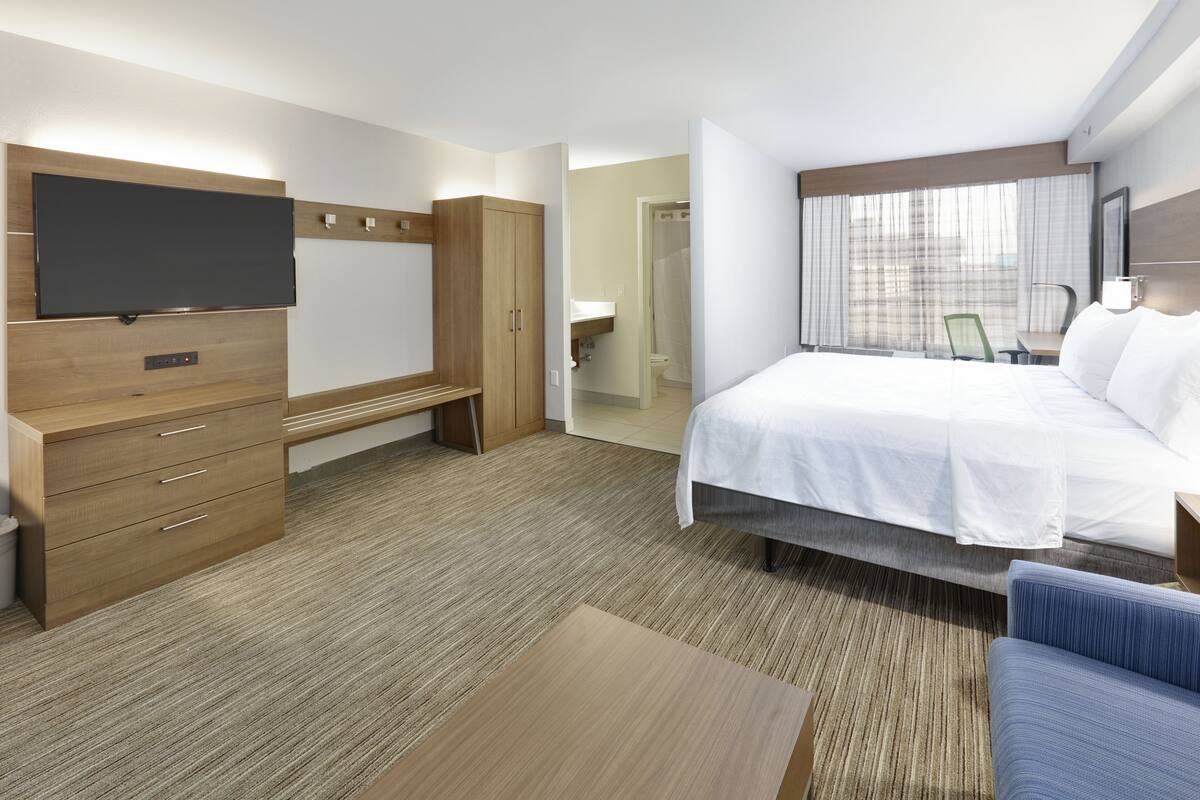 A hotel room with a bed, a desk with drawers, a television, and a window with curtains.