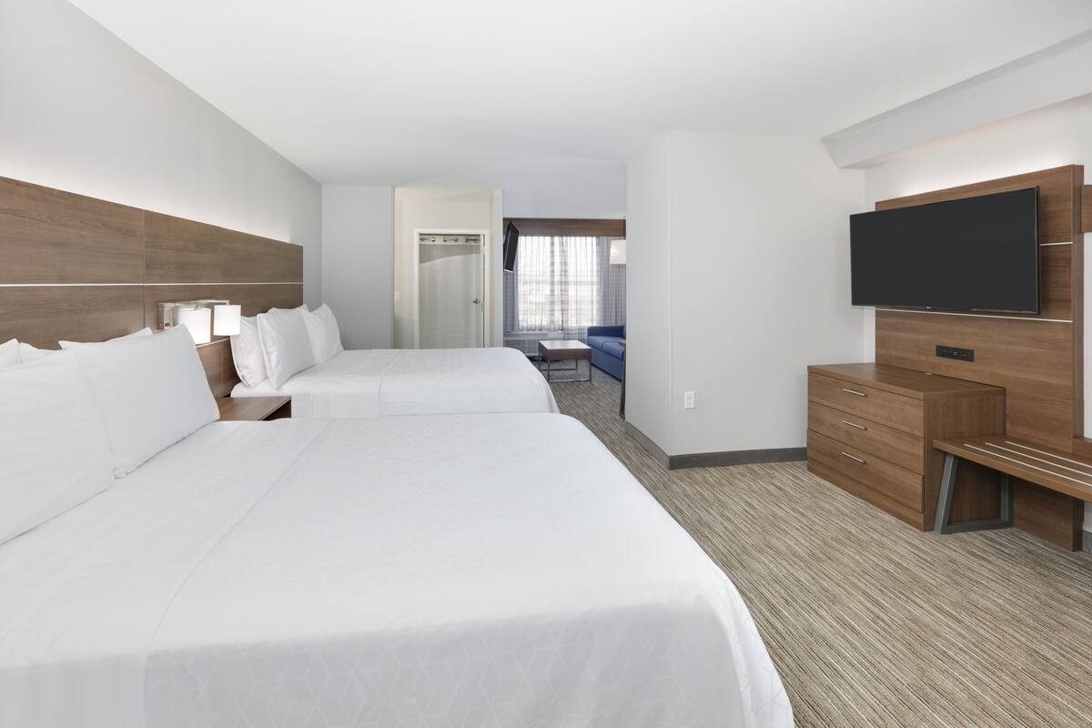 A hotel room with two beds, a TV, a desk, and a seating area.