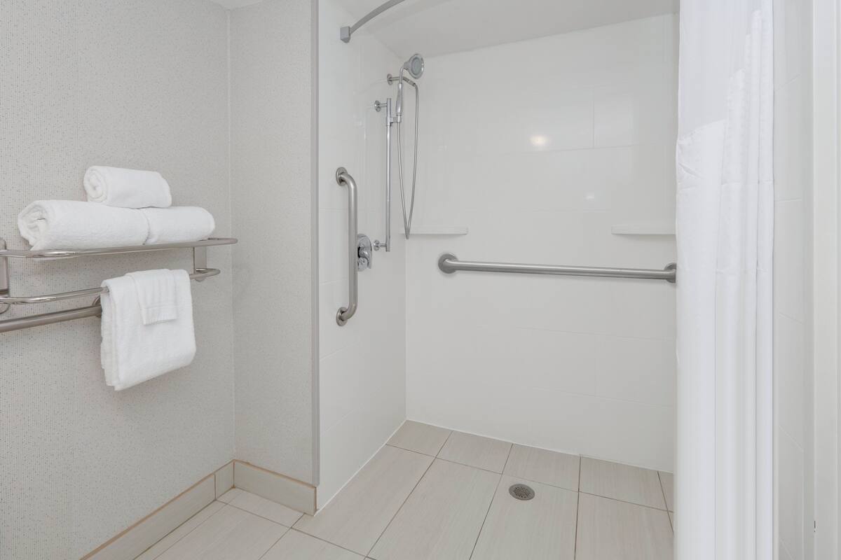 A shower with a grab bar, a towel rack with towels, and a showerhead.