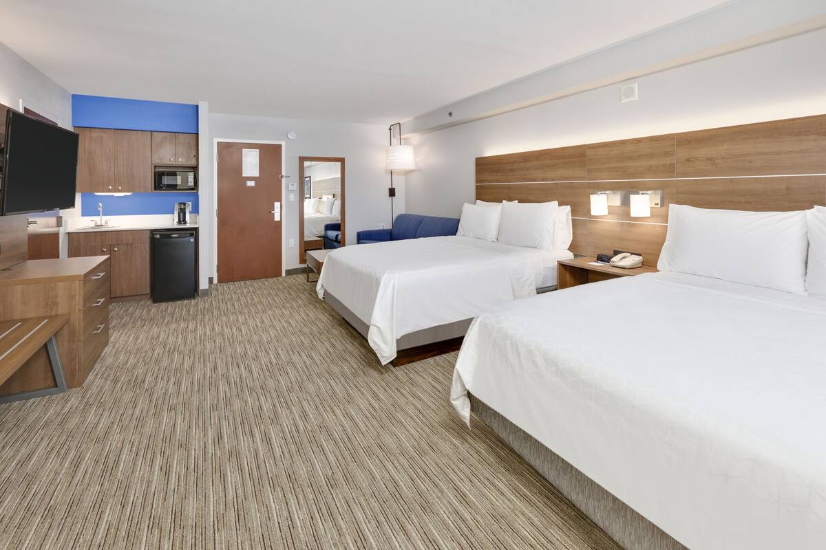 A hotel room with two beds, a desk with a flat-screen TV, a microwave, and a coffee maker.