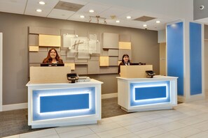 A hotel reception area with two reception desks, a wall-mounted sign, and a blue door. - Holiday Inn Express & Suites Irving Conv Ctr - Las Colinas by IHG (Irving)
