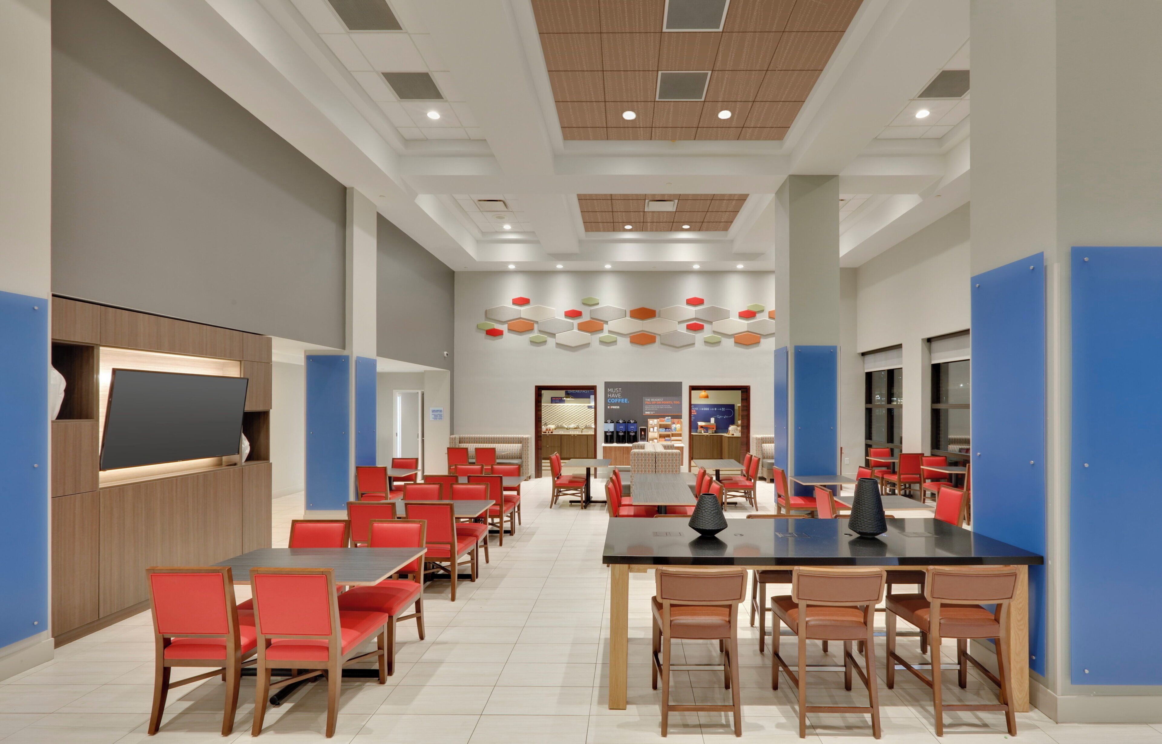 A spacious indoor area with multiple tables and chairs, a counter with a display, and a ceiling with recessed lighting.