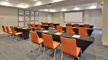 A conference room with multiple tables and chairs, a projector screen, and framed artwork on the walls.