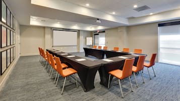 A conference room with a long table, orange chairs, a projector, a whiteboard, and framed pictures on the wall.