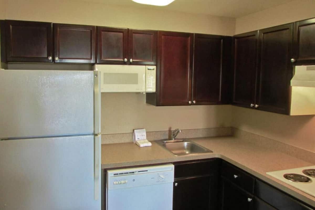 A kitchen with dark wooden cabinets, a white refrigerator, a microwave, a dishwasher, and a sink.