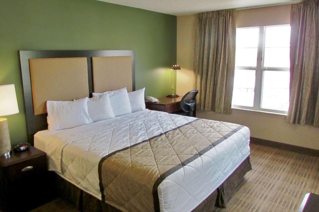 A hotel room with a large bed, a desk, a chair, a lamp, and a window with curtains.