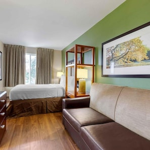 Ein Hotelzimmer mit einem Bett, einem Sofa, einem Nachttisch aus Holz, einer Lampe und einem Bild an der Wand.